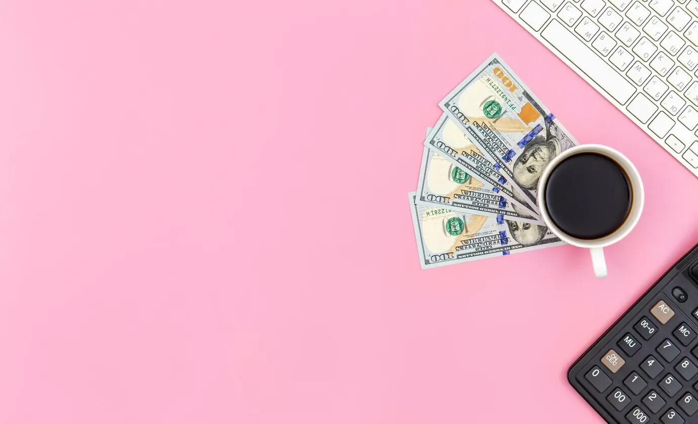 Чашка кофе и долларовые купюры на розовом фоне, вид сверху.